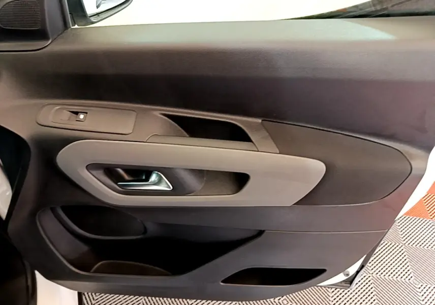 Vue rapprochée de la porte avant gauche intérieure du Peugeot Rifter blanc, avec poignée argentée et panneau noir/gris.