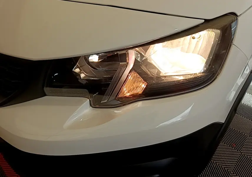Gros plan sur le phare avant droit allumé d’un Peugeot Rifter blanc, mettant en valeur les détails du bloc optique.