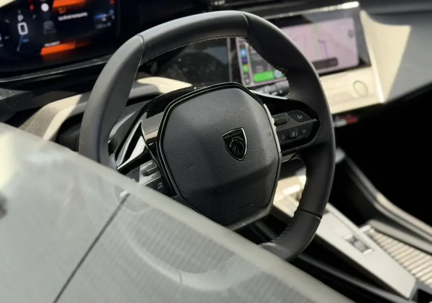 Vue rapprochée du volant cuir noir avec logo Peugeot, tableau de bord digital et écran tactile du Peugeot 308 SW 2025.