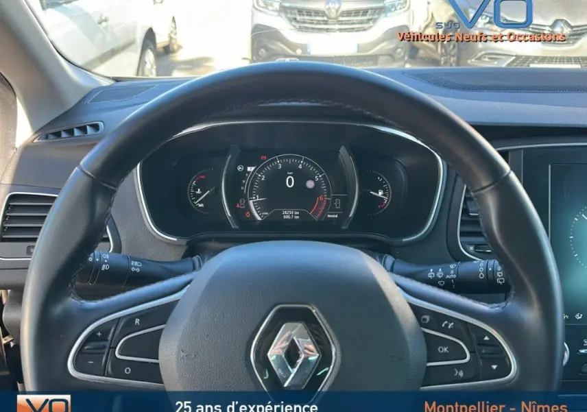 Vue depuis le siège conducteur sur le volant cuir et le tableau de bord numérique d'une Renault Mégane IV beige de 2017.