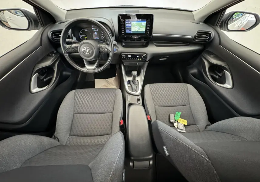 Vue intérieure frontale de la Toyota Yaris hybride 2022, tableau de bord noir avec écran tactile et sièges gris.