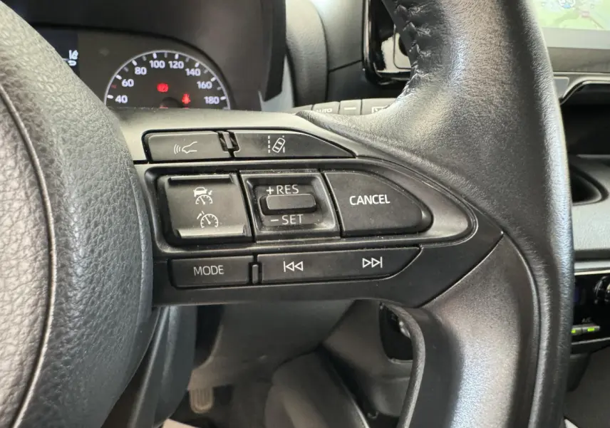 Gros plan sur les commandes du volant cuir noir de la Toyota Yaris Hybride 2022, avec affichage partiel du tableau de bord.