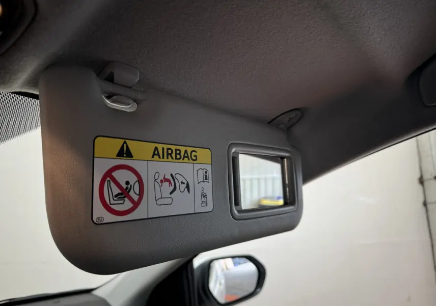 Détail du pare-soleil côté conducteur gris avec avertissement airbag et miroir intégré dans une Toyota Yaris blanche 2022.
