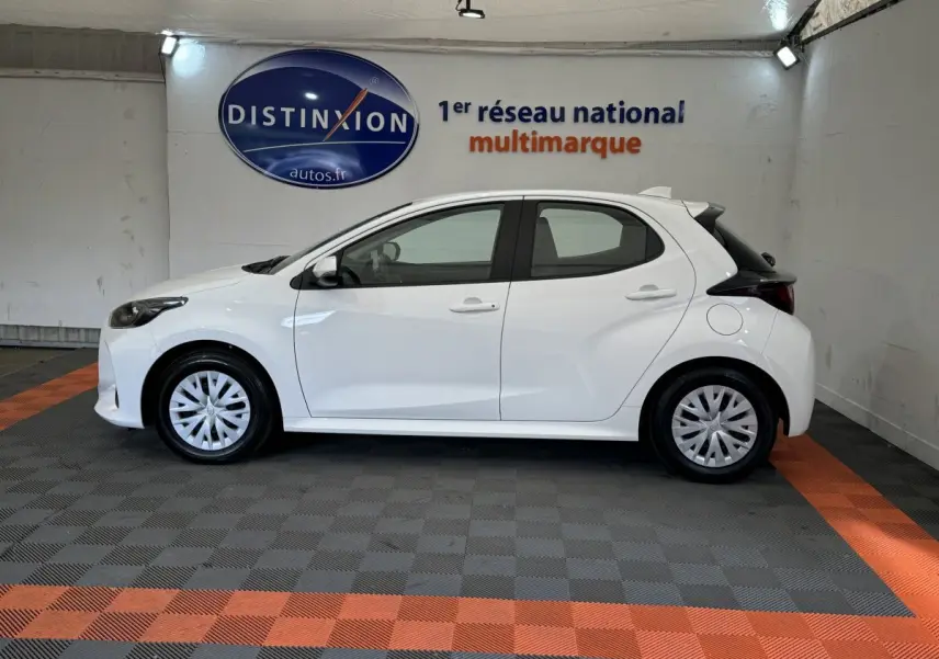 Profil côté gauche d'une Toyota Yaris blanche hybride 2022, avec jantes et feux arrière distinctifs visibles en intérieur showroom.
