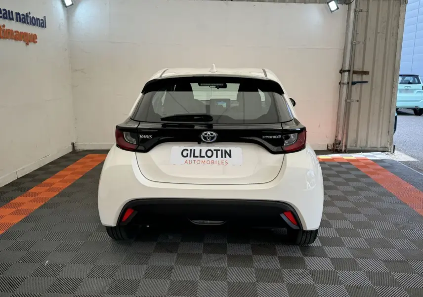 Vue arrière d'une Toyota Yaris hybride blanche avec bande noire distinctive sur le hayon et feux arrière intégrés.