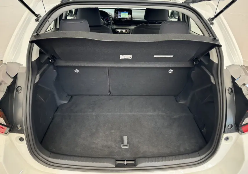 Coffre ouvert d'une Toyota Yaris blanche vue de l'arrière, avec banquette arrière et tableau de bord visible.