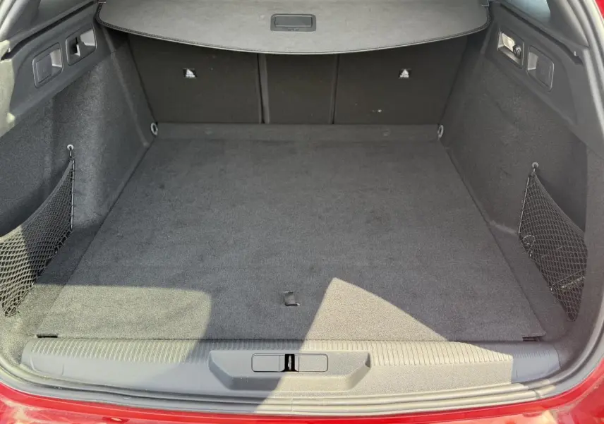 Coffre ouvert vu de l'arrière d'une Peugeot 308 SW Rouge Elixir, avec tapis de sol et filet de rangement latéral.