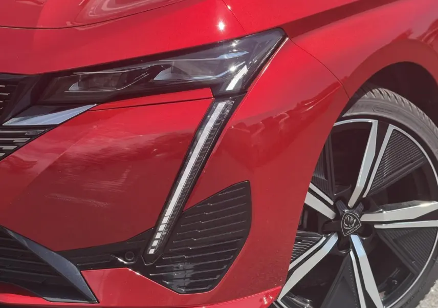 Gros plan sur l'avant droit rouge Elixir du Peugeot 308 SW 2024, mettant en valeur le phare LED et la jante alliage 18''.
