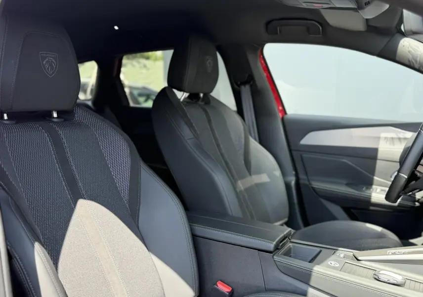 Vue intérieure côté conducteur montrant les sièges avant noirs avec logo Peugeot brodé sur les appuie-têtes.