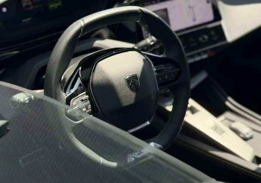 Gros plan sur le volant cuir noir du Peugeot 308 SW 2024 avec tableau de bord numérique et console centrale beige.
