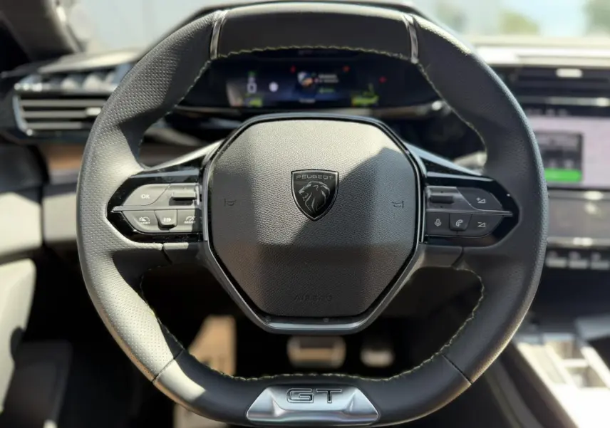 Volant cuir noir au design compact avec logo Peugeot et badge GT, vue frontale centrée sur le poste de conduite.