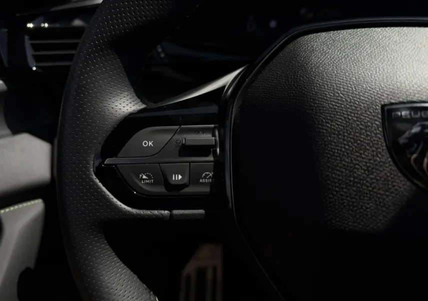 Gros plan sur le volant cuir perforé de la Peugeot 308 SW 2024 avec commandes intégrées et logo Peugeot visible.