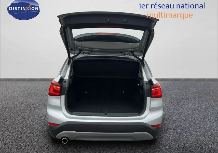 Vue arrière d’un BMW X1 gris argent métal 2018 avec le coffre ouvert, montrant l’espace de chargement vide.