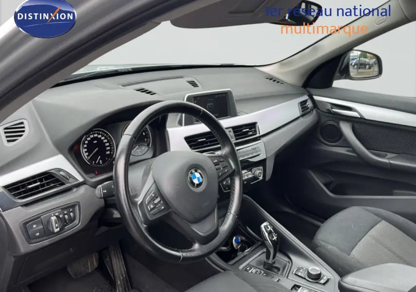 Vue intérieure côté conducteur du tableau de bord et volant d'une BMW X1 18i gris argent de 2018.