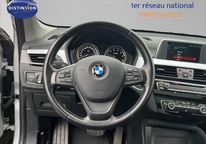 Vue intérieure centrée sur le volant noir de la BMW X1 18i 2018 avec tableau de bord et écran multimédia visibles.