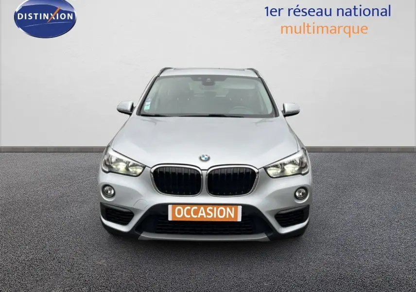 Vue frontale d'un BMW X1 gris argent métallisé avec calandre noire et phares allumés sur fond neutre.