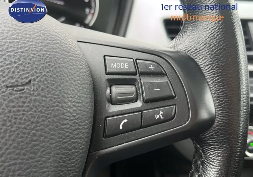 Gros plan sur les commandes du volant en cuir noir du BMW X1 18i gris argent, mettant en valeur les boutons multifonctions.