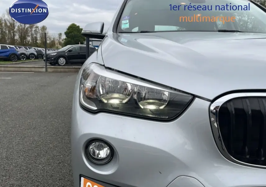 Vue avant gauche rapprochée d’un BMW X1 gris argent métallisé avec phares allumés et calandre noire distinctive.