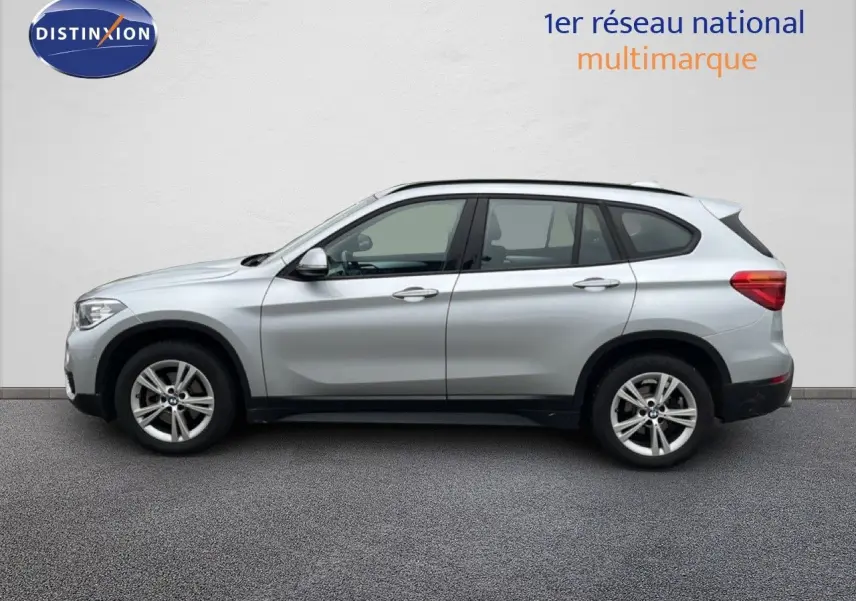 Profil côté gauche d'un BMW X1 18i gris argent métallisé, avec jantes alliage et lignes épurées visibles.