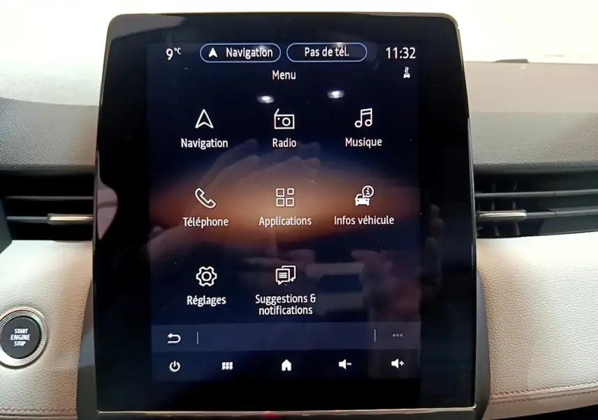 Écran tactile central allumé avec menu principal dans l'habitacle clair d'une Renault Clio Initiale Paris E-TECH 140 orange.