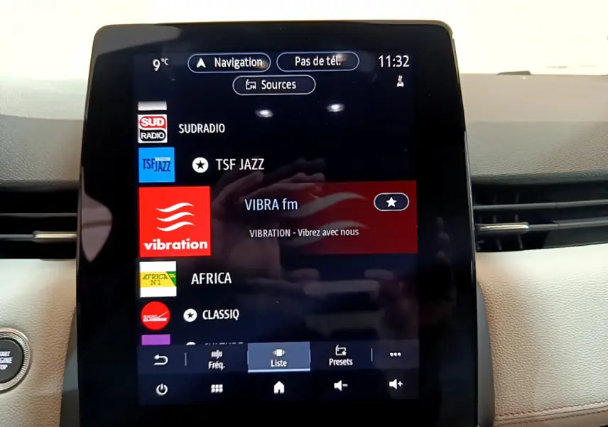 Écran tactile central affichant les stations radio dans l'habitacle clair d'une Renault Clio Initiale Paris E-TECH 2021