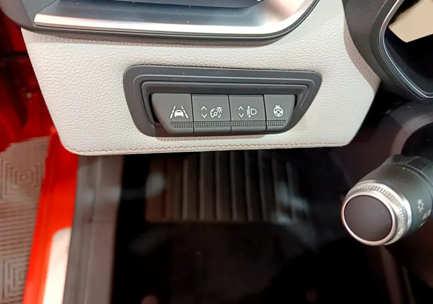 Gros plan sur les commandes d'assistance et éclairage sous le tableau de bord beige d'une Renault Clio Initiale Paris orange.