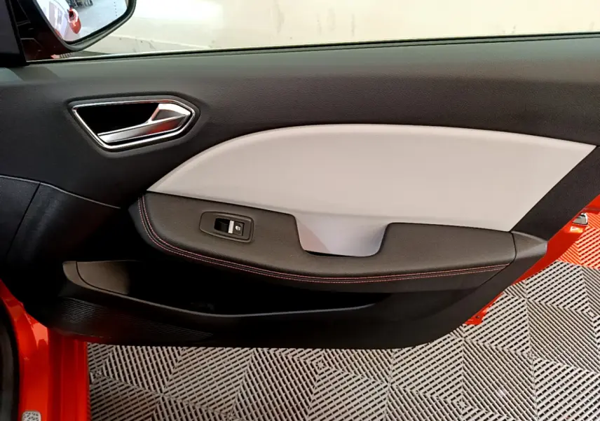 Gros plan sur la porte côté gauche de la Renault Clio Initiale Paris orange, avec garniture bicolore et bouton de vitre électrique.