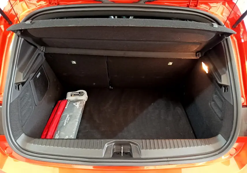 Coffre ouvert vu de l'arrière d'une Renault Clio Initiale Paris orange, avec trousse de sécurité visible à gauche.