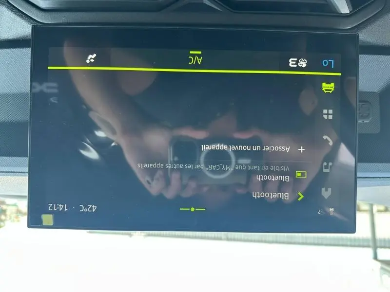 Écran tactile central du tableau de bord du Dacia Duster blanc, affichant les réglages de climatisation et Bluetooth.