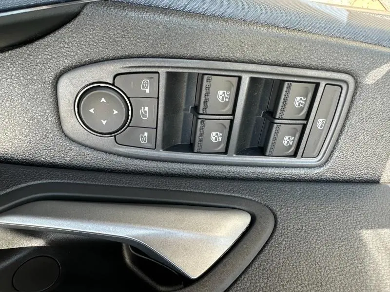 Vue rapprochée des commandes des vitres et rétroviseurs côté gauche intérieur du Dacia Duster blanc 2025.