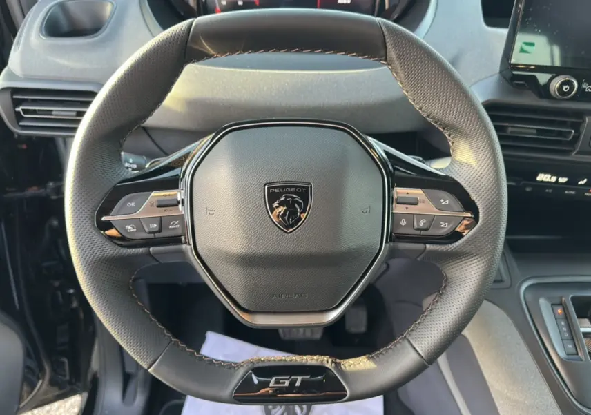 Vue rapprochée du volant cuir multifonctions Peugeot Rifter GT Plus noir avec logo central et commandes intégrées.
