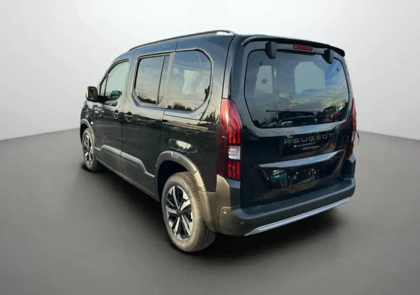 Vue 3/4 arrière droite du Peugeot Rifter noir perla nera avec barres de toit et jantes alu 17 pouces visibles.