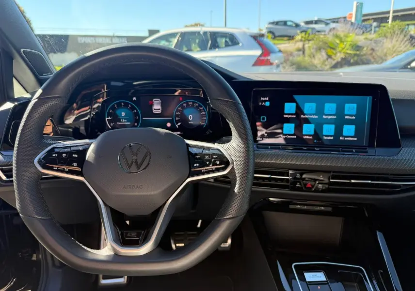 Vue intérieure centrée sur le volant cuir multifonction et l'écran tactile du tableau de bord d'une Volkswagen Golf noire.