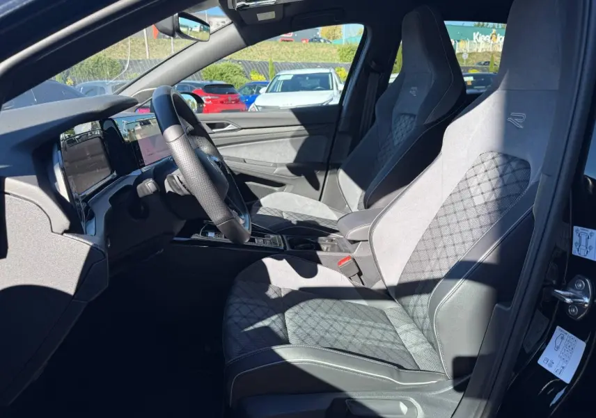 Vue intérieure côté conducteur de la Volkswagen Golf 1.5 eTSI R-Line 2024 avec sièges sport en tissu gris et volant cuir multifonction.