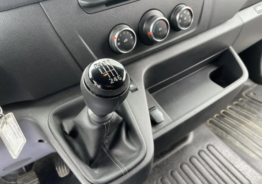 Gros plan sur le levier de vitesses manuel noir et la console centrale du Renault Master blanc, avec commandes de climatisation visibles.