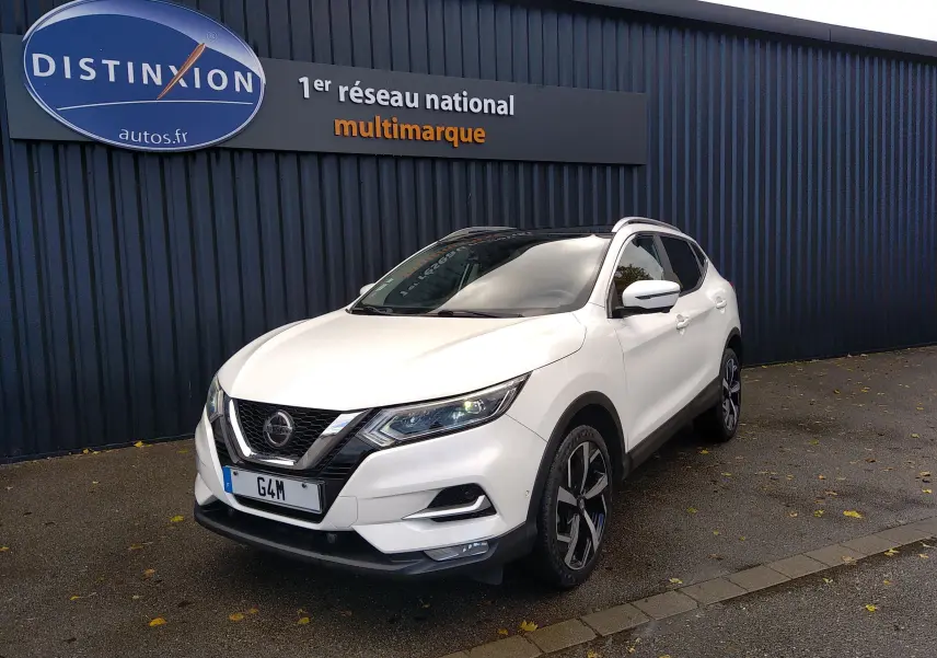 Nissan Qashqai blanc vue 3/4 avant droit, avec jantes alliage noires et calandre chromée, stationné devant un mur bleu.