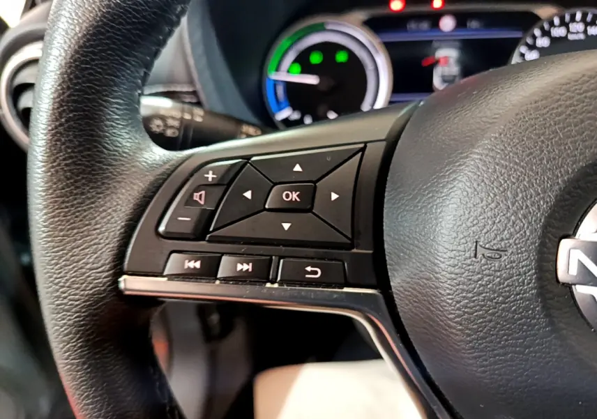 Gros plan sur le volant cuir noir à commandes multifonctions du Nissan Juke Hybrid 143 Business+ gris foncé, tableau de bord en arrière-plan.