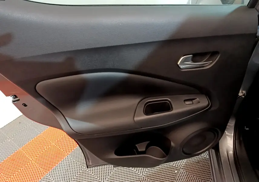 Porte intérieure côté gauche du Nissan Juke Hybrid 143 Business+ 2023 en gris foncé avec poignée et commandes de vitre.