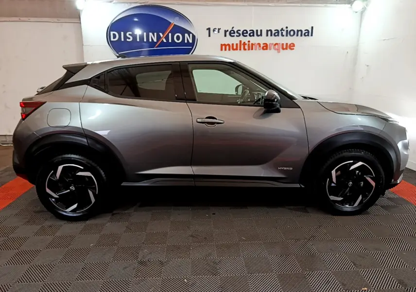 Profil côté gauche du Nissan Juke Hybrid 143 Business+ gris foncé avec jantes noires et logo hybrid visible.
