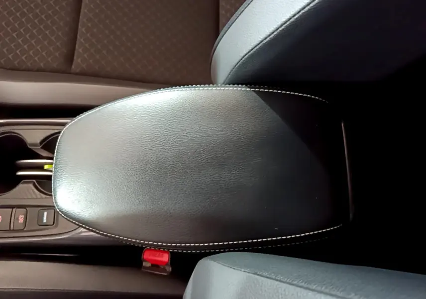 Accoudoir central en cuir noir avec surpiqûres blanches, entouré des sièges et console centrale du Nissan Juke Hybrid 2023.