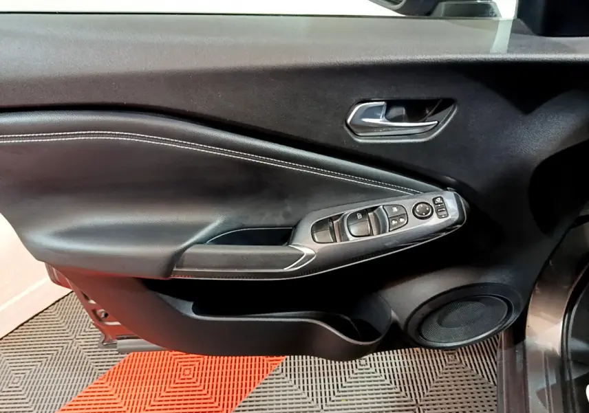 Gros plan sur la porte côté conducteur du Nissan Juke Hybrid gris foncé, montrant les commandes électriques et le haut-parleur intégré.