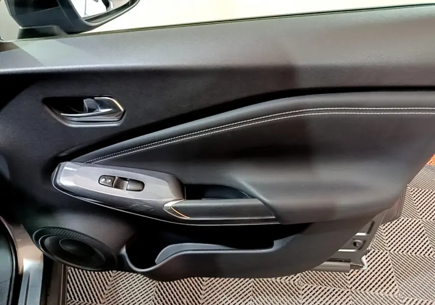 Gros plan sur la porte côté gauche intérieure du Nissan Juke Hybrid gris foncé avec commandes de vitres et haut-parleur.