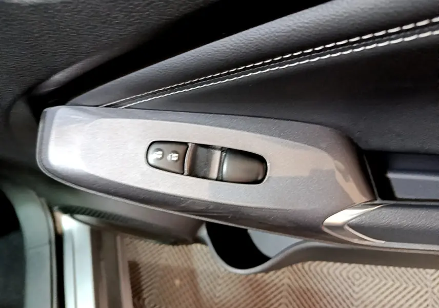 Gros plan sur la commande de verrouillage des portes côté conducteur dans l'habitacle noir du Nissan Juke Hybrid 2023.