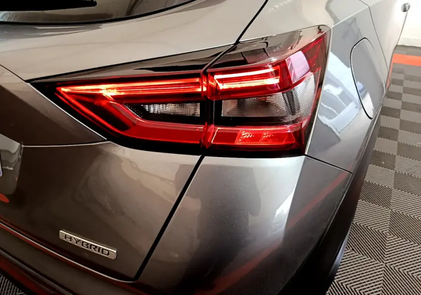 Gros plan sur le feu arrière droit rouge et le badge Hybrid d'un Nissan Juke gris foncé 2023.