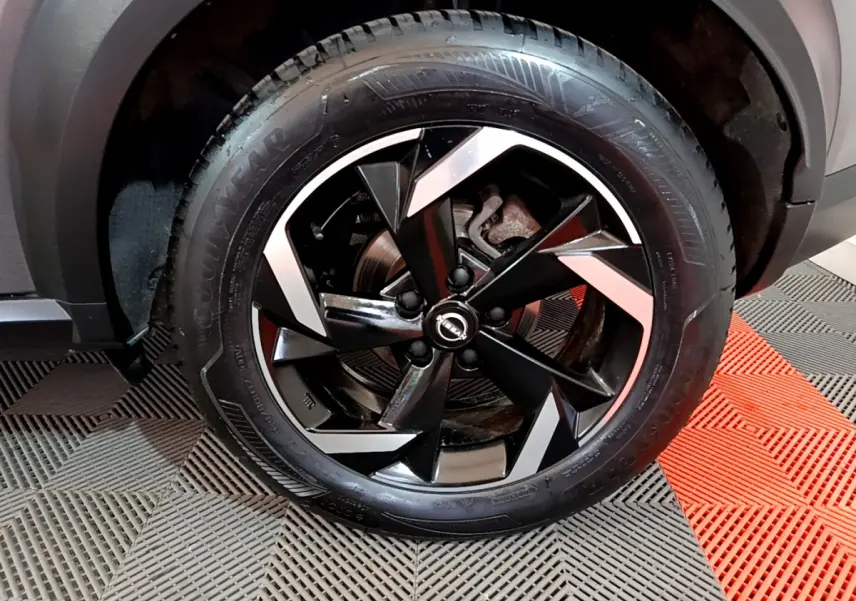 Gros plan sur la roue avant droite du Nissan Juke Hybrid 143 Business+ gris foncé avec jante noire et argentée.