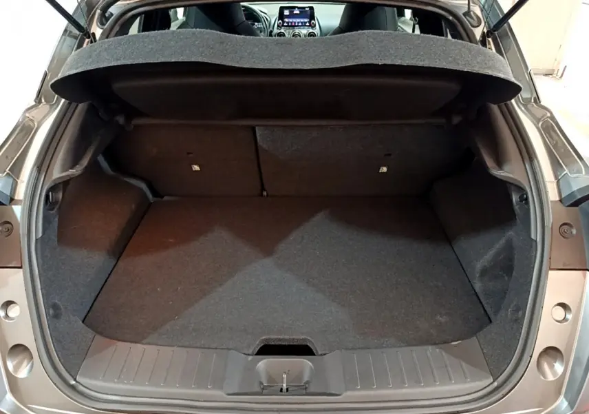 Coffre ouvert vu de l'arrière d'un Nissan Juke Hybrid 143 Business+ gris foncé, intérieur noir et tablette de coffre visible.