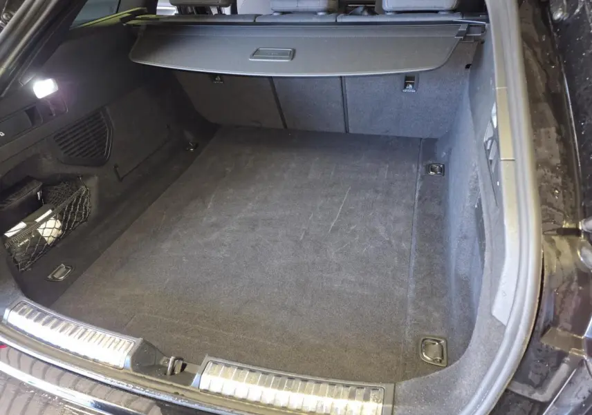 Coffre ouvert vu de l’arrière d’une Audi A5 Avant noir, avec tapis de sol et filet de rangement latéral.