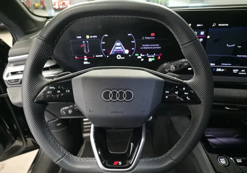 Volant sport en cuir avec logo Audi et S, vue frontale du poste de conduite numérique de l'Audi A5 Avant noir 2025.
