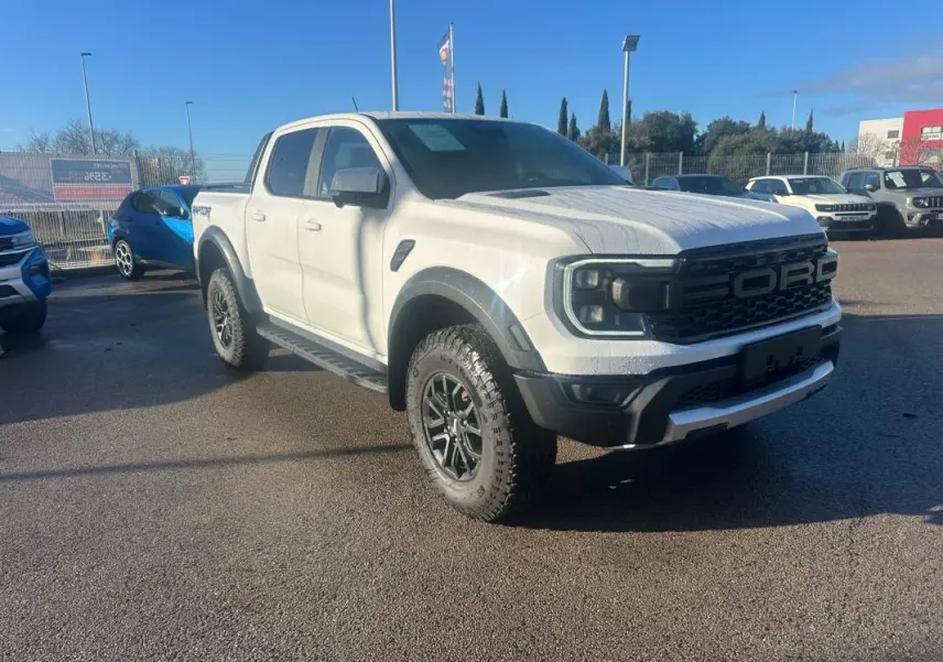 Ford Ranger Raptor blanc en 3/4 avant droit avec jantes alliage noires et marchepieds visibles sur parking.