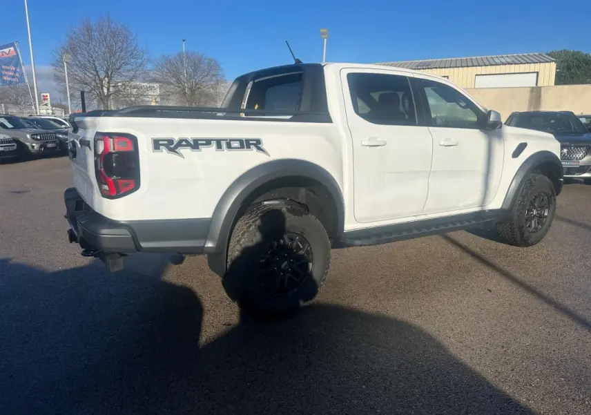 Ford Ranger Raptor blanc en vue 3/4 arrière droit, avec logo Raptor et jantes alliage noires visibles.